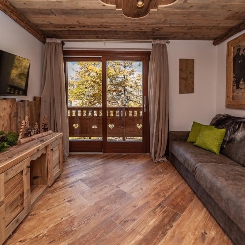 Cozy rustic living room featuring a wooden door, gray couch, wooden cabinets, and warm lighting with a tree view outside.