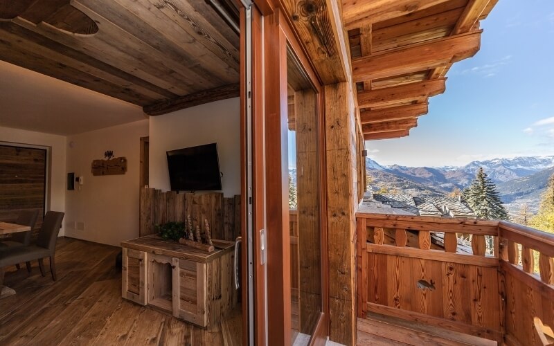 Room with wooden decor, open door to balcony, mountain view, dining table, and decorative cabinet with pinecones.