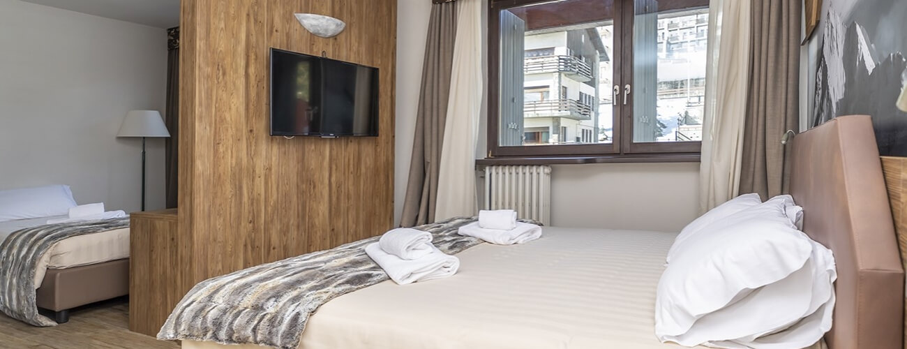 Hotel room with two beds, a flat-screen TV, a window with curtains, and neutral decor in beige and brown tones.