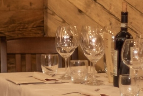 Tavolo da ristorante elegante con calici di vino, bottiglia e segnaposto arancioni su tovaglia bianca.