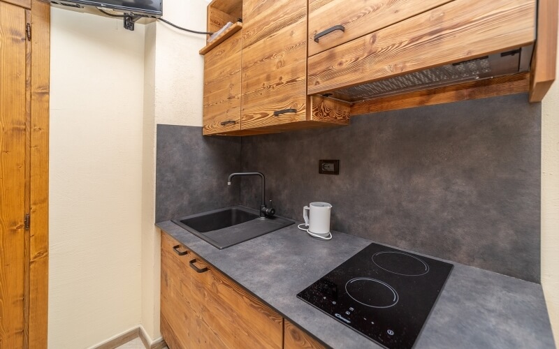 Piccola cucina con armadietti in legno, piano in marmo grigio, piano cottura nero, lavandino e tazza bianca sul bancone.
