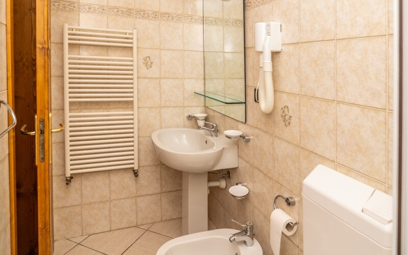 Bagno compatto con WC, lavabo, porta asciugamani e specchio, decorato con piastrelle chiare e motivo floreale.