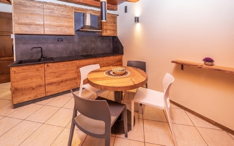 Modern kitchen and dining area with a round wooden table, four chairs, black countertop, and warm wooden cabinets.