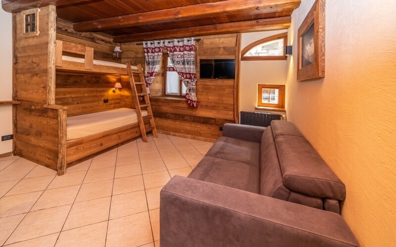 Cozy room with a light wood bunk bed, comfortable couch, patterned curtain window, and tiled floor.