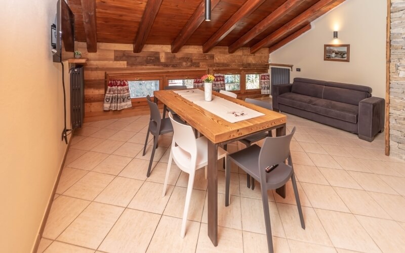 Living room with dining area, featuring a wooden table, gray couch, and mounted TV, all in a calm, modern design.