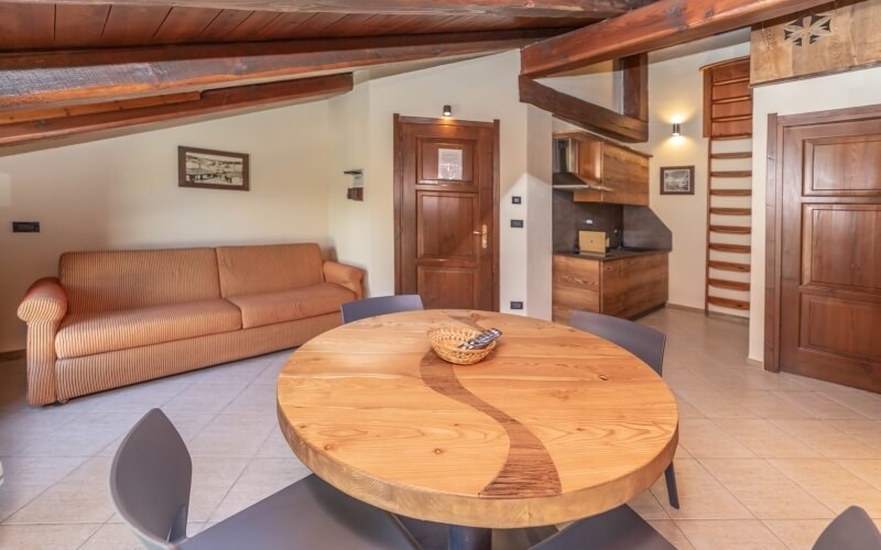 A cozy living room and kitchen area featuring a round wooden dining table with a unique design, soft lighting, and framed pictures.