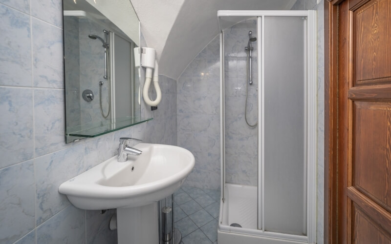 Bagno compatto con piastrelle blu, lavabo bianco, specchio e doccia in vetro, atmosfera intima e accogliente.