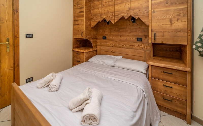 Camera da letto accogliente con letto centrale, comodini, armadi, pareti beige e un oggetto verde con fiori bianchi.