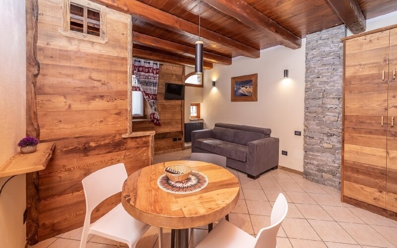 Cozy rustic living room and dining area with wooden decor, gray couch, round table, and warm lighting.