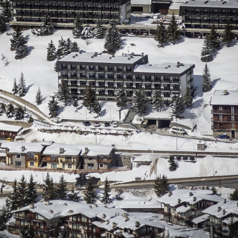 Snowy landscape with buildings, evergreen trees, and a clear road, creating a serene winter resort atmosphere.