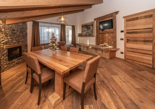 Una sala da pranzo accogliente con tavolo in legno, camino, TV, divano e decorazioni rustiche.
