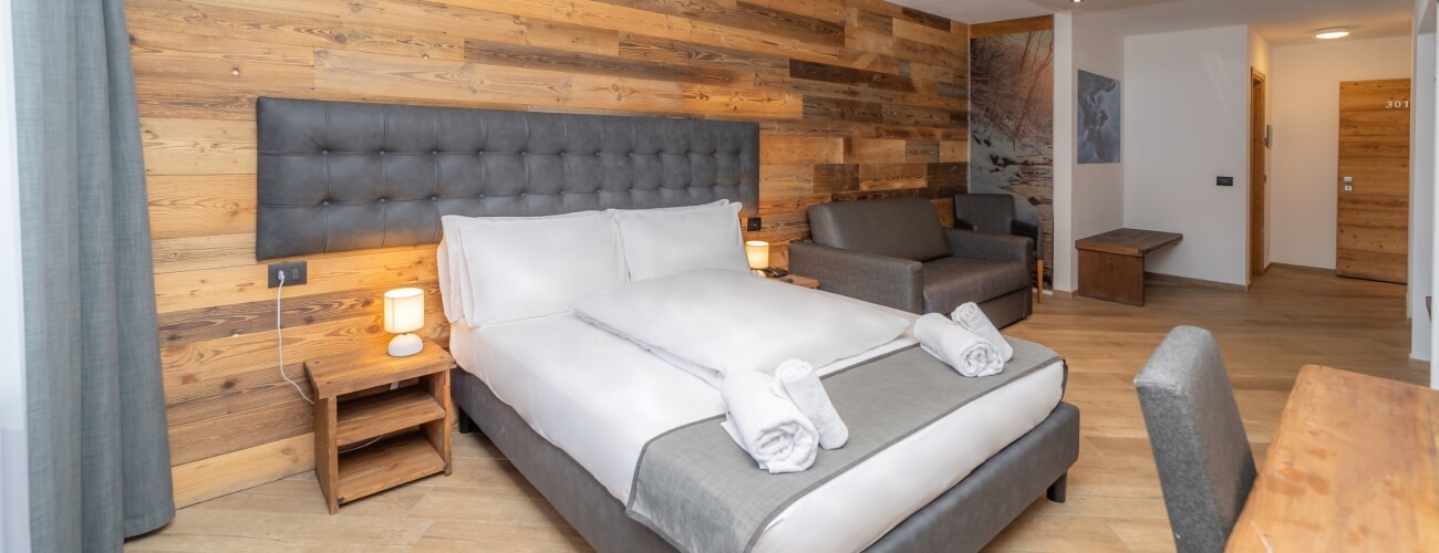 Modern hotel room with a large bed, gray armchair, wooden tables, and a door marked "301," exuding comfort and cleanliness.