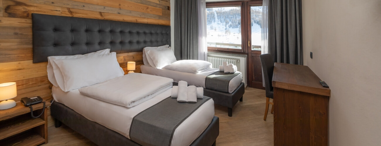 Cozy hotel room with two beds, a desk, and a window view of a snow-covered field, featuring rustic wooden accents.