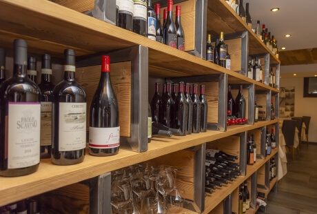 Wine rack made of light wood with metal poles, displaying various wine bottles and glasses in an upscale setting.