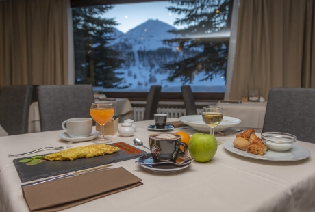 Breakfast table set in a restaurant with food items, orange juice, coffee, and a view of snow-capped mountains.