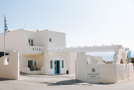 Edificio bianco con insegna "HOTEL KATIKIES EMERALD", bandiera greca, ingresso coperto con porta blu e finestre.