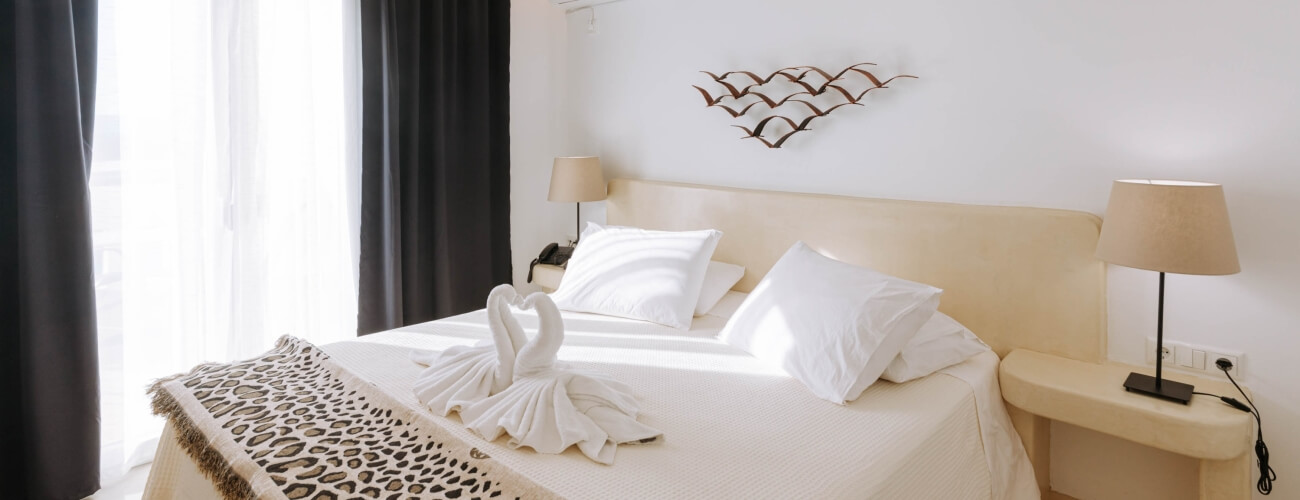 Camera serena con letto grande, lenzuola bianche, sculture decorative e asciugamani a forma di cigno. Atmosfera invitante.