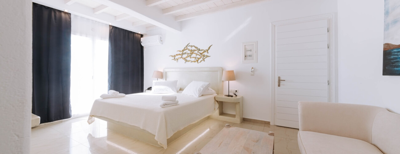 Serene interior with a white bed, beige couch, natural light, and abstract art, creating a cozy, inviting atmosphere.