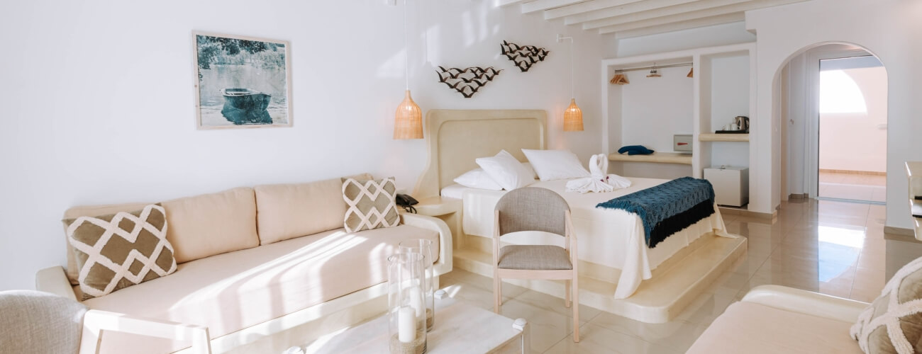 Camera d'albergo accogliente con letto, divano e sedia, decorata in toni bianchi e beige, con arte e dettagli eleganti.