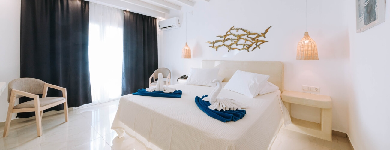 Camera d'albergo serena con letto bianco, arte dorata, sedie, tende grigie e illuminazione calda. Atmosfera rilassante.