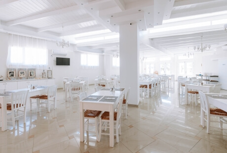 Large, bright room with white walls, tables, chairs, a central pillar, and windows, suggesting a dining or event space.