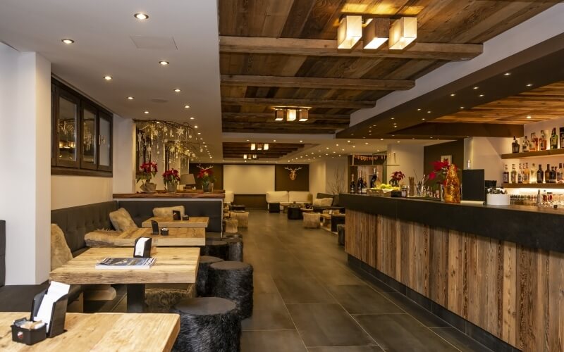 Modern restaurant/bar with cozy seating and bar areas, featuring wooden decor, warm lighting, and a brown color scheme.