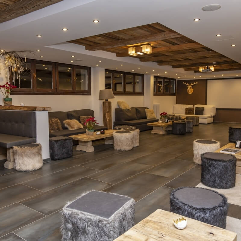 Modern living room with rustic decor, featuring gray and white couches, fur-covered tables, and a mounted deer head.