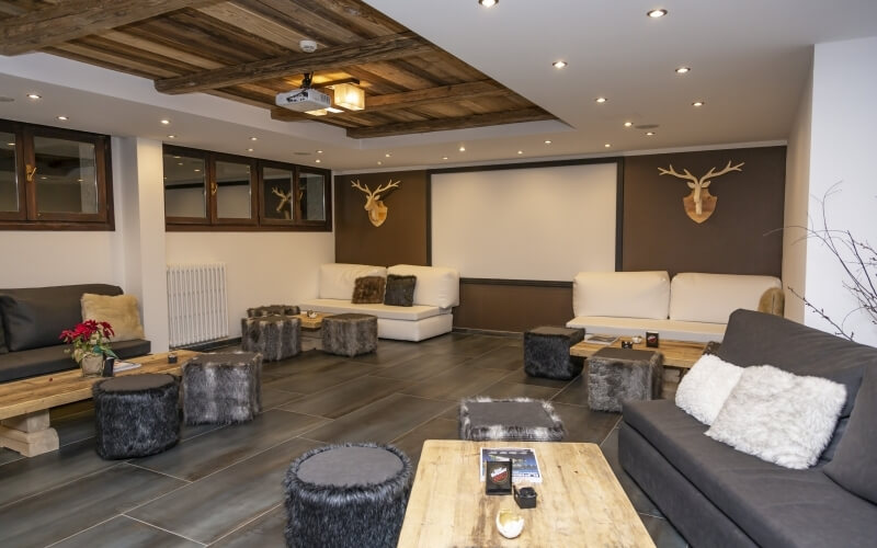 Modern living room with rustic elements, featuring a projector, gray and white couches, fur ottomans, and antler decor.