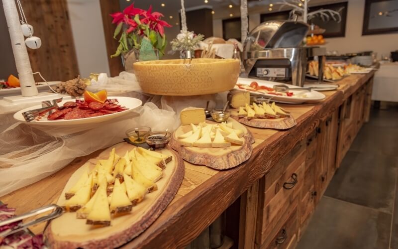 A wooden buffet table with cheese, meat, fruit, sauces, and festive decorations, set in a warmly lit environment.