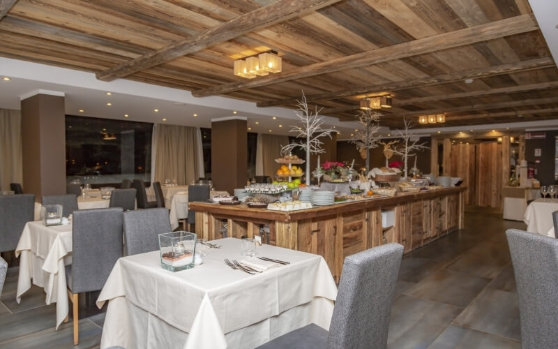 Ristorante elegante con tavolo buffet in legno, piatti assortiti, decorazioni bianche e tavoli ben apparecchiati.