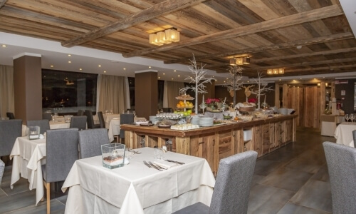 Spacious restaurant dining room with rustic wooden accents, long table, gray chairs, and warm recessed lighting.