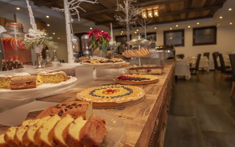 Buffet table with assorted pastries, desserts, and festive decorations, set in a bright dining area with wooden beams.