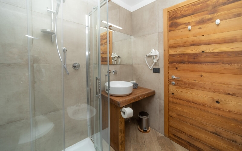 A clean bathroom featuring a glass-enclosed shower, white sink, wooden door, and beige tiled walls.