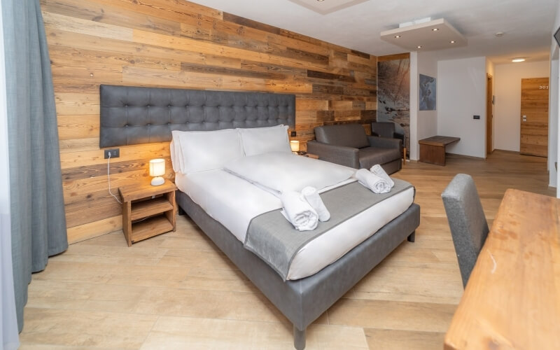 Serene hotel room with a gray and white color scheme, featuring a large bed, nightstand, couch, and wooden accents.