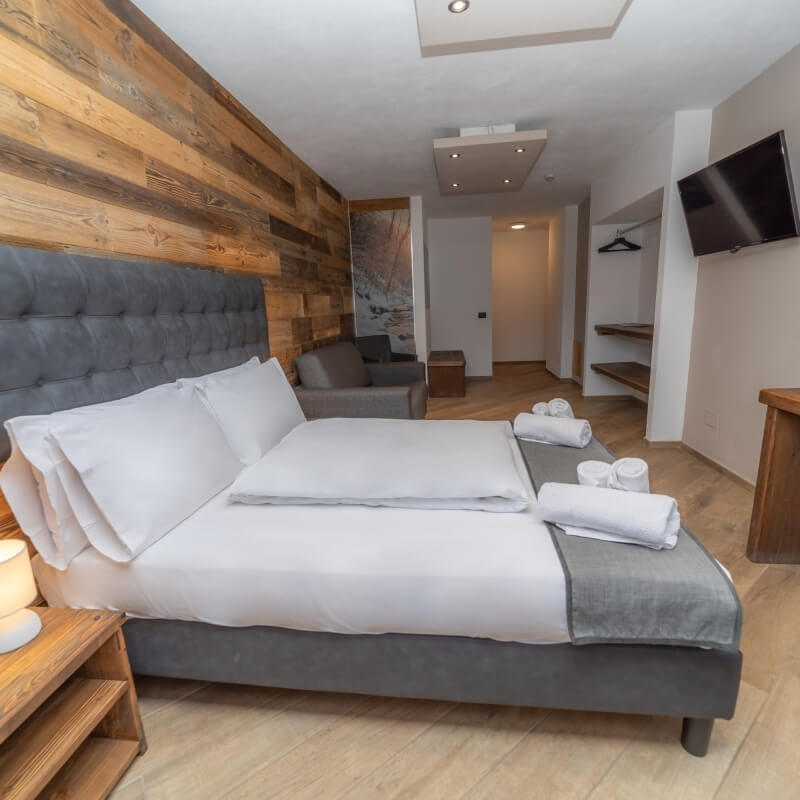 Modern hotel room with a bed, nightstand, TV, and wooden accents; clean and organized atmosphere.