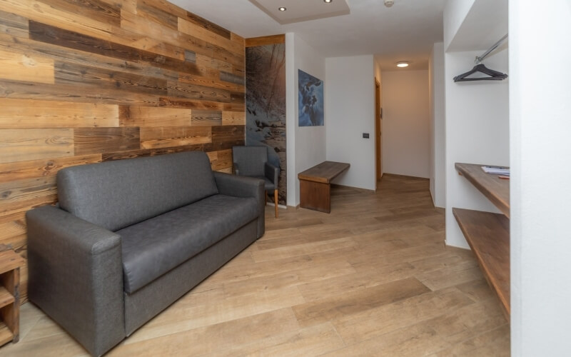 Modern room with wood plank wall, gray couch, wooden table, and shelf, featuring a sliding glass door to the right.