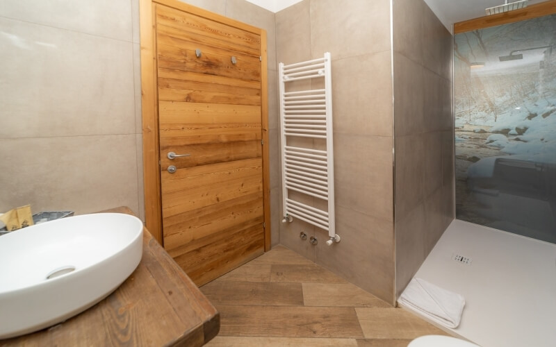 Modern bathroom featuring a wooden door, white sink with yellow bottles, towel rack, and glass-enclosed shower area.