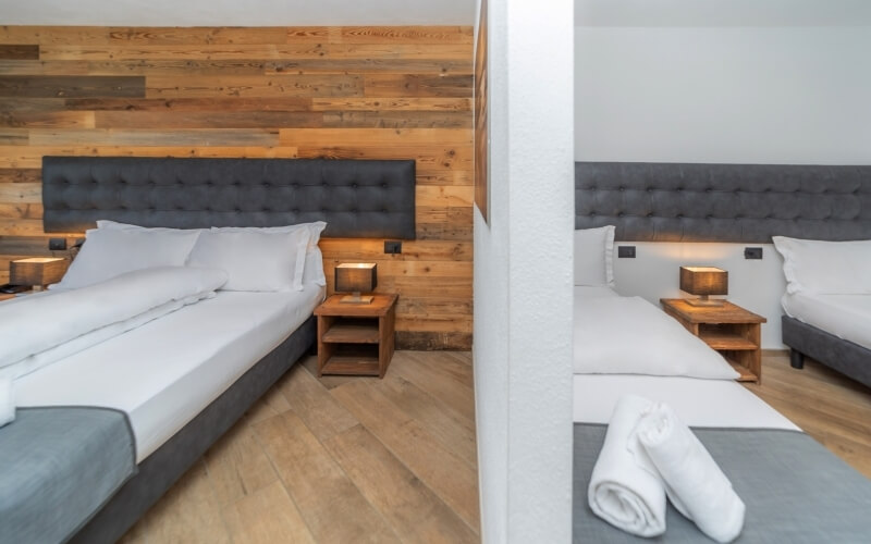 Dual view of a hotel room with two beds, gray headboards, white bedding, and a light wood accent wall, emphasizing minimalism.