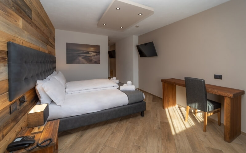 Modern hotel room with a bed, desk, chair, soothing colors, and a serene sunset photograph above the bed.