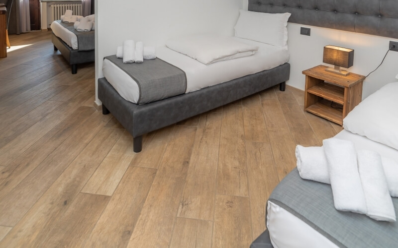 Cozy bedroom with two beds, gray headboards, white linens, and a warm wooden floor, creating an inviting atmosphere.