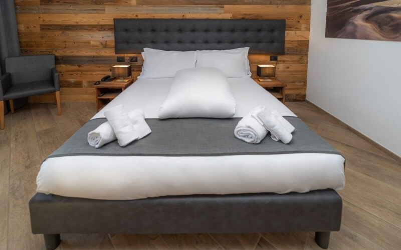 A clean bedroom featuring a gray upholstered bed, white linens, nightstands with lamps, and decorative elements.