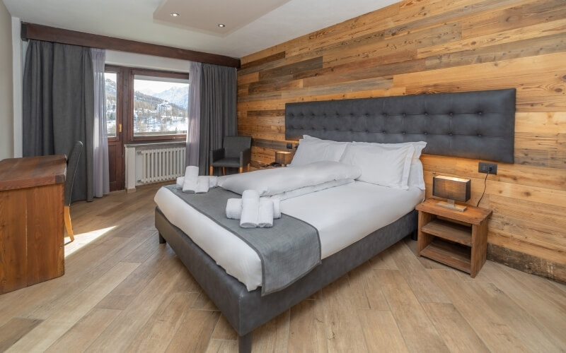 Serene hotel room with a gray queen bed, mountain view, cushioned chairs, and warm wood accents, exuding comfort and relaxation.