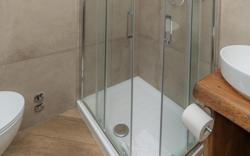 Modern bathroom with glass shower, white toilet, wooden vanity, and beige tile walls, creating a clean and calming atmosphere.