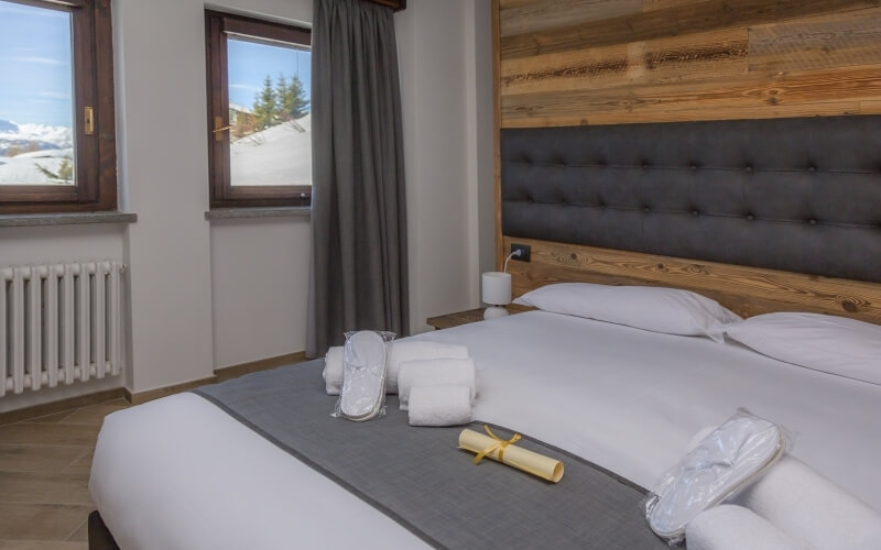 Serene hotel room with a cozy bed, mountain view, and warm wood accents, featuring pillows, slippers, and a ribboned scroll.