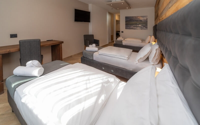 A well-lit hotel room with two beds, a desk, a chair, and modern decor, featuring light wood flooring and white walls.