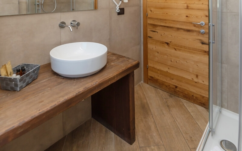 Minimalist bathroom featuring a wooden table with a white oval sink and a glass shower door on the right.