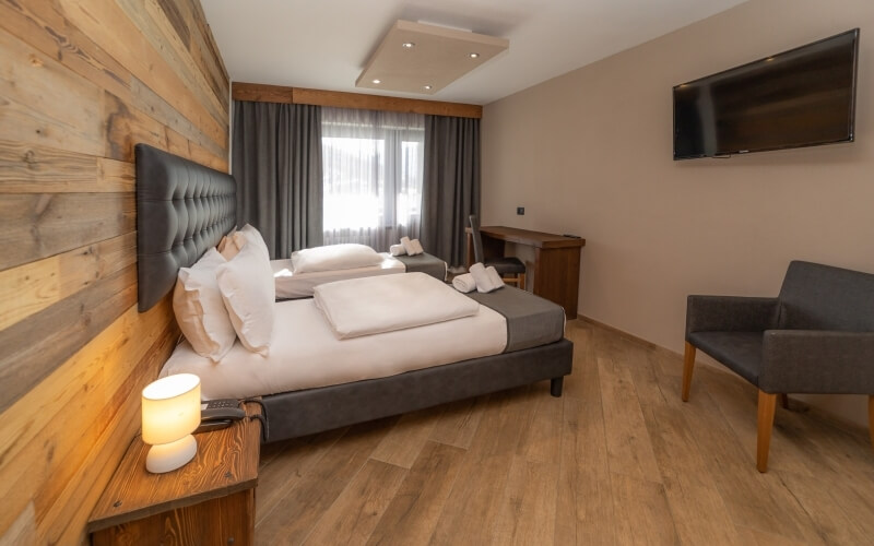 Modern hotel room with two beds, a TV, beige walls, light wood floor, and gray curtains, designed for comfort.