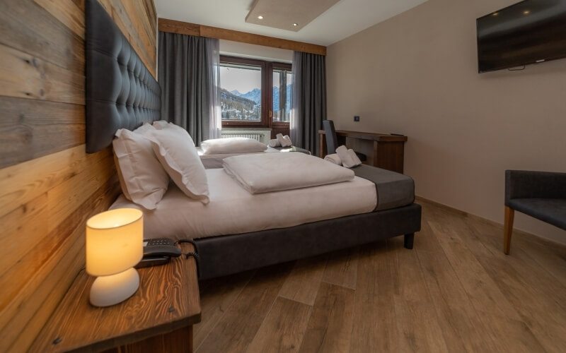 Cozy hotel room with two beds, a desk, television, and mountain view, featuring light wood paneling and beige walls.