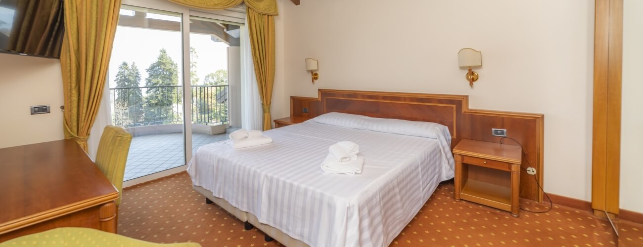 Hotel room featuring a double bed, nightstand, desk, balcony door, and orange carpet with yellow diamond patterns.