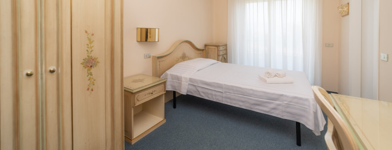 Serene hotel room with a bed, nightstand, dresser, and desk, featuring warm colors and soft lighting for relaxation.